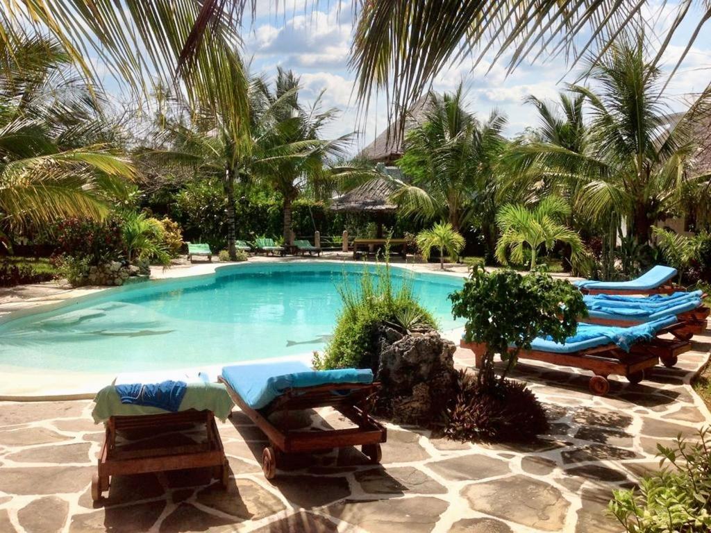 a swimming pool with lounge chairs and palm trees at Spacious accessible house in Watamu, shared pool in Watamu