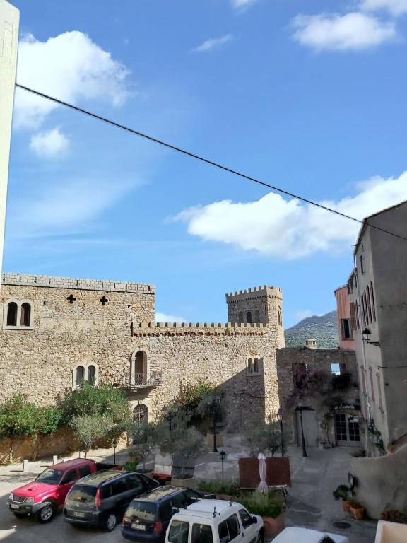 un grand bâtiment en pierre avec des voitures garées dans un parking dans l'établissement Appartement charmant à Algajola avec terrasse, à Algajola