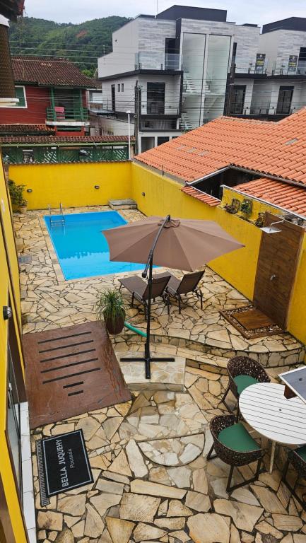 a patio with an umbrella and chairs and a pool at Pousada Bella Juquehy in Juquei