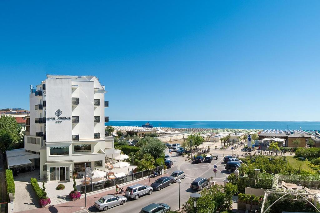 a building with cars parked in a parking lot next to the ocean at Hotel Oriente in Milano Marittima
