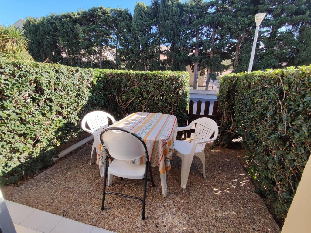 une table et des chaises assises sur une terrasse avec des buissons dans l'établissement Appartement 3 pièces pour 4 avec piscine, terrasse et parking privé à 400m de la plage à Argelès-sur-Mer - FR-1-776-21, à Argelès-sur-Mer