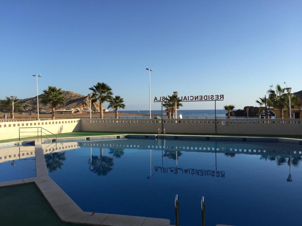 a swimming pool next to a beach with palm trees at Apartamento en Residencial La Isla in Puerto de Mazarrón
