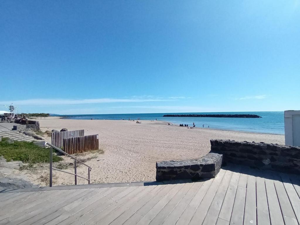 une plage de sable avec une promenade en bois et l'océan dans l'établissement Appartaucap34, au Cap d'Agde