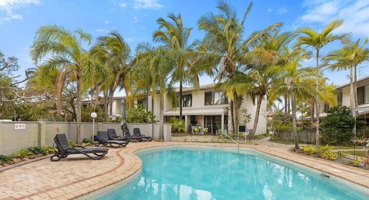 a swimming pool with two chairs and palm trees at Noosa Sound - 2brm Townhouse in Noosaville