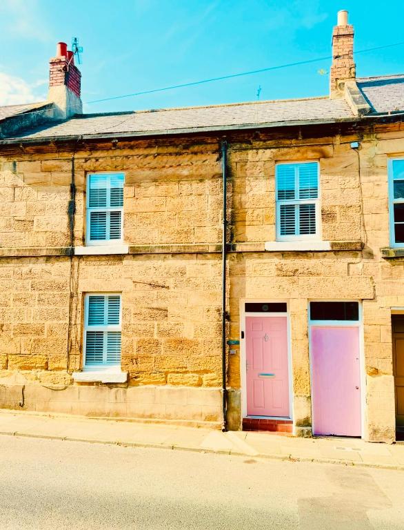 an old brick building with two pink doors at HomeDecor Cottages - Castle Walk House in Alnwick