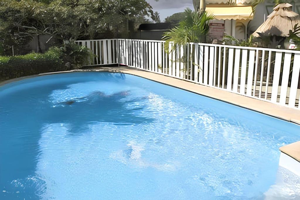 a large blue swimming pool with a white fence at Bungalow charmant à Sainte-Rose avec piscine partagée in Sainte-Rose