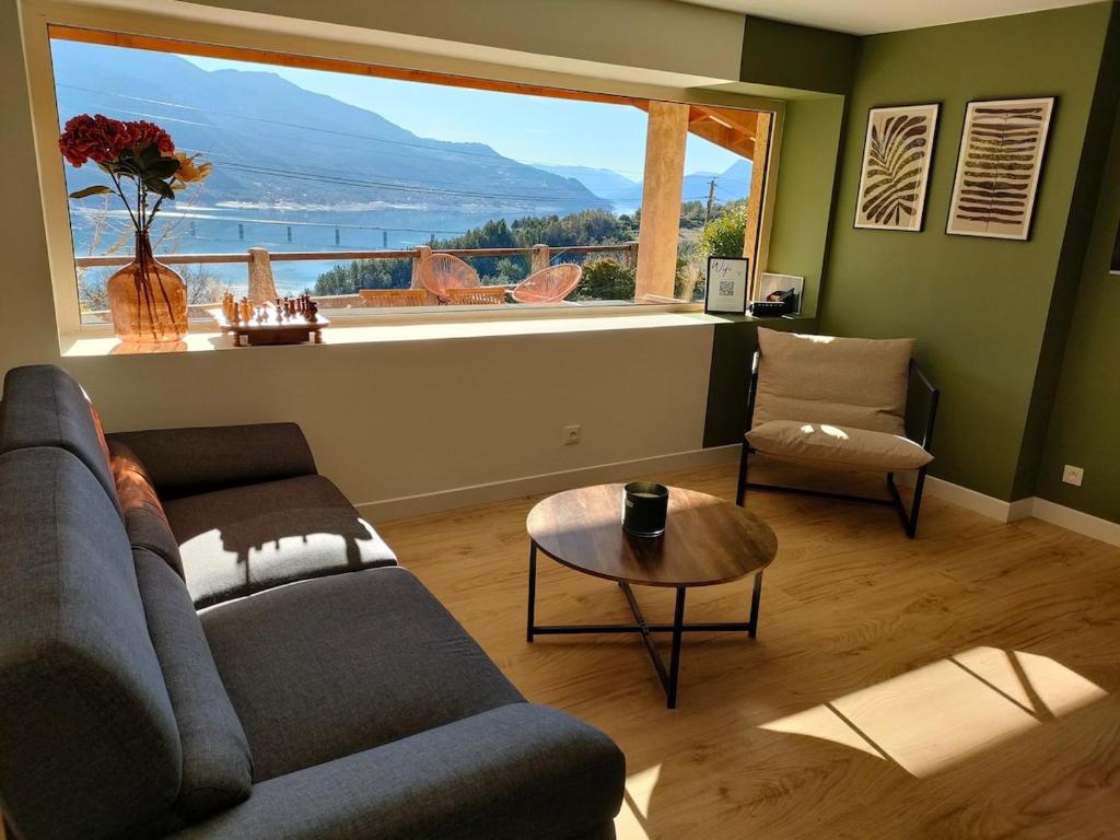 - un salon avec un canapé, une table et une grande fenêtre dans l'établissement La Maison du Plongeoir 14 pers grande terrasse vue lac de Serre Ponçon, à Savines