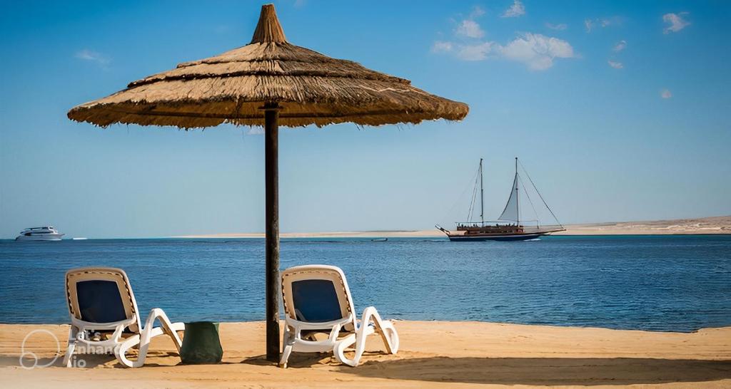 two chairs and an umbrella on a beach with a boat at Al-Dora Resort Hurghada in Hurghada
