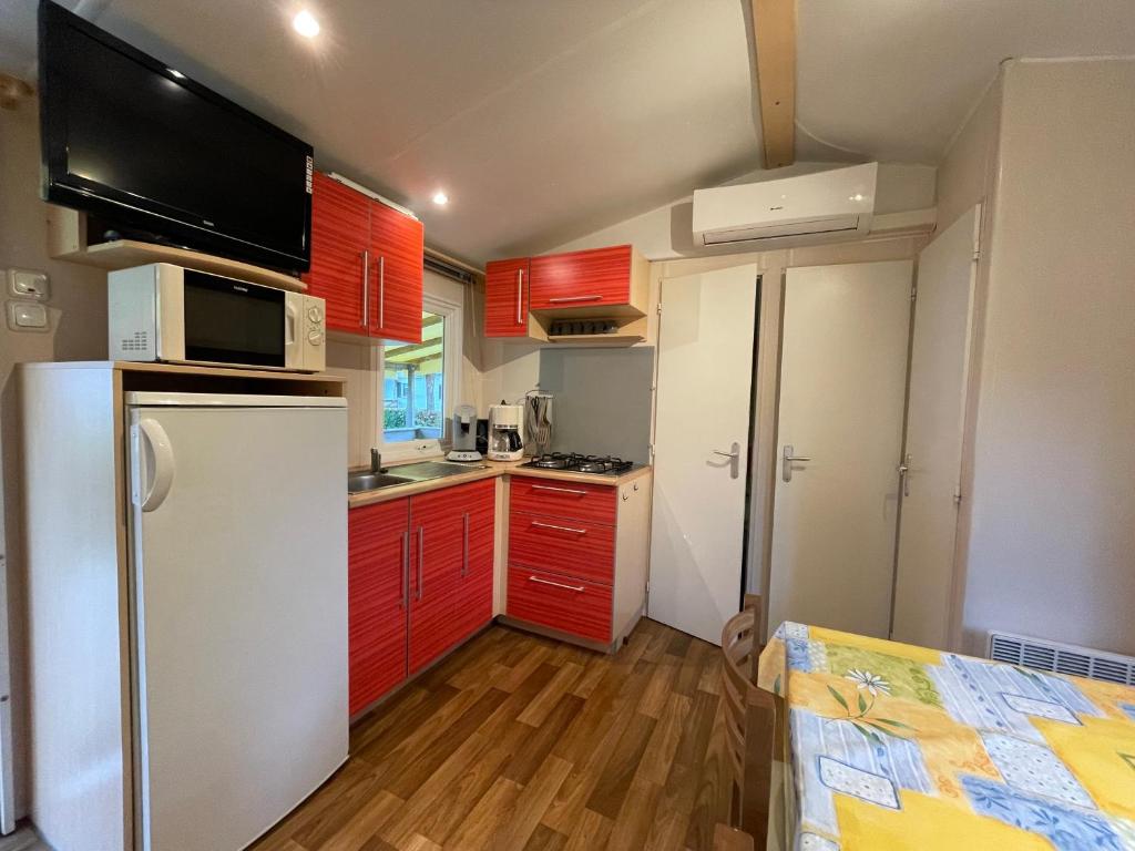 a small kitchen with red cabinets and a white refrigerator at Bungalow N52 - 6 personnes au calme - Camping Le Ried Boofzheim in Boofzheim