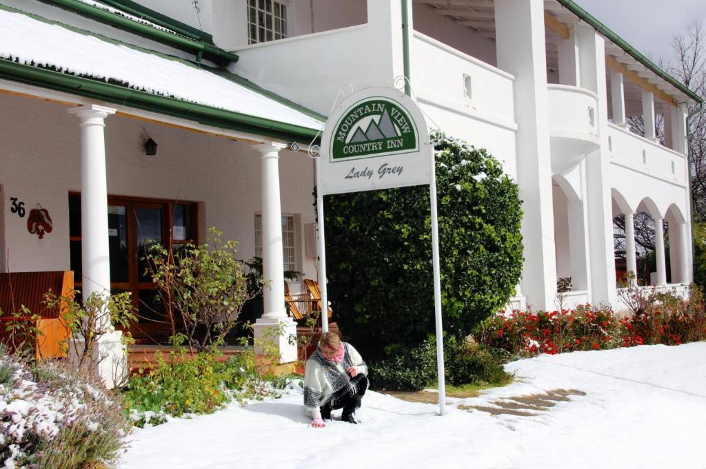 Eine Frau kniet neben einem Schild vor einem Haus in der Unterkunft Mountain View Country Inn in Lady Grey