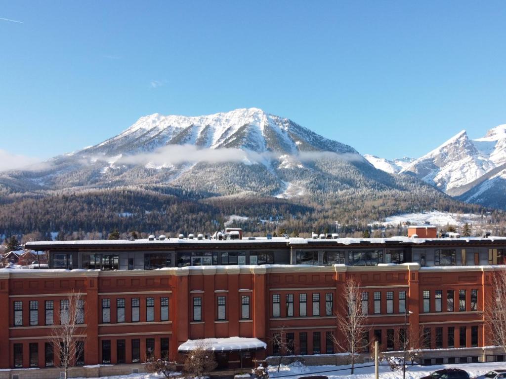 a building with a snow covered mountain in the background at The Historic 901 Condos In the Heart of Fernie in Fernie