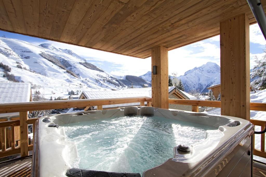 a hot tub on a deck with snow covered mountains at Odalys Chalet L'Ours Brun in Les Deux Alpes