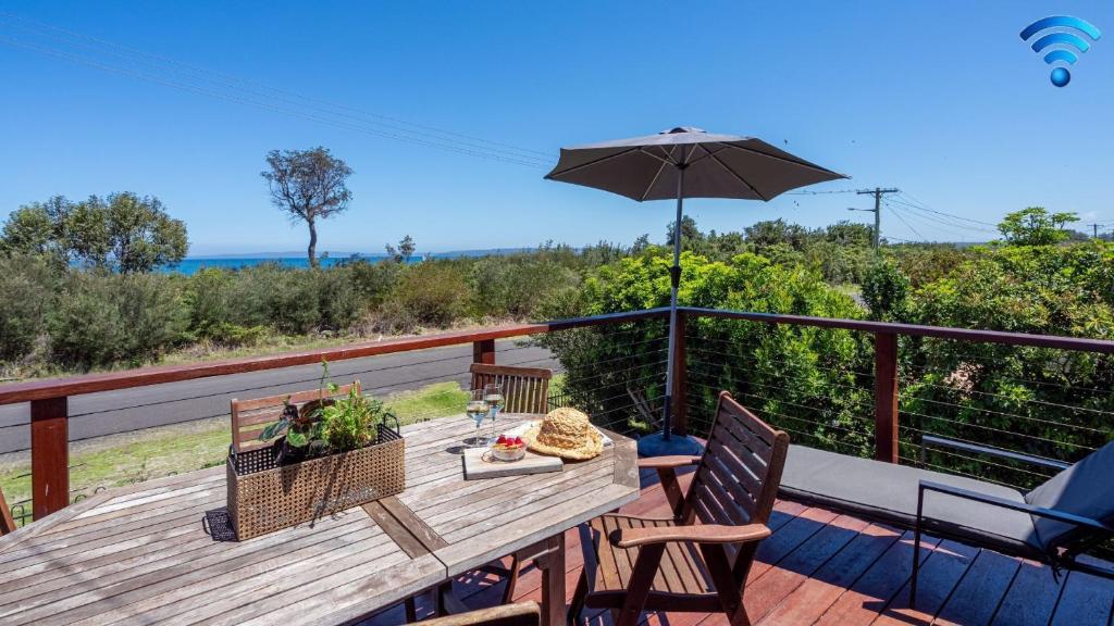 una mesa de madera con sillas y una sombrilla en una terraza en Thistledoo, en Callala Beach
