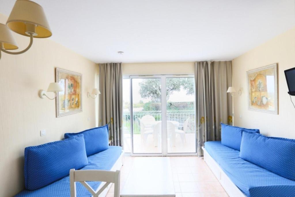 un salon avec des canapés bleus et un balcon dans l'établissement Résidence le Hameau des Issambres - maeva Home - Studio 5 personnes - Sélection MAE-0621, aux Issambres