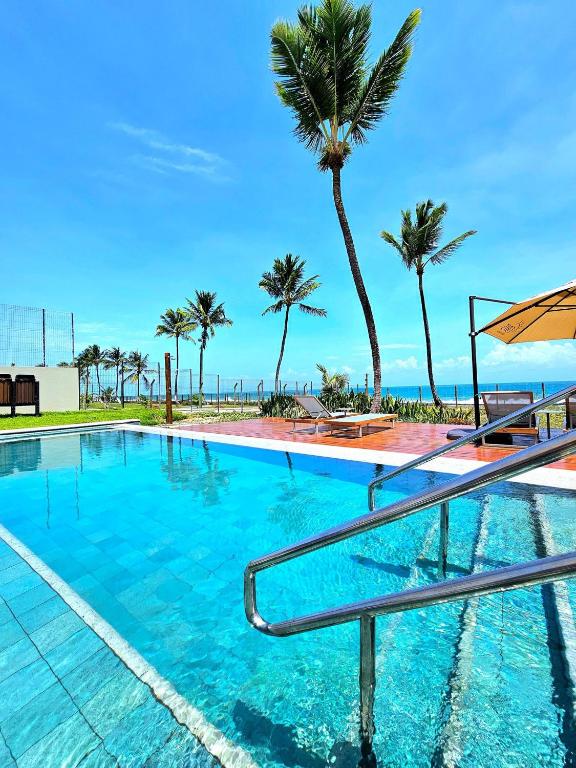 a swimming pool with palm trees and the ocean at Sofisticação e Luxo à Beira-mar no Cais Eco em Muro Alto by HM in Porto De Galinhas