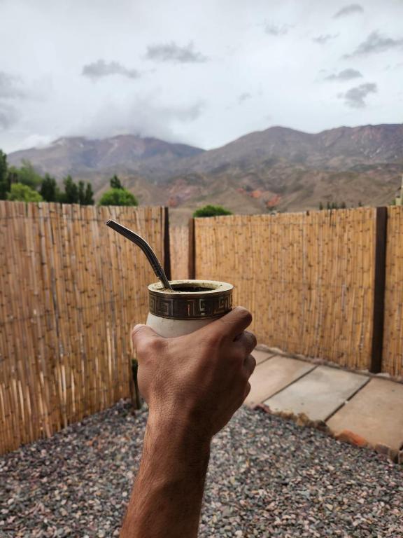 a person holding a cup of coffee in front of a fence at La Gauda in Huacalera
