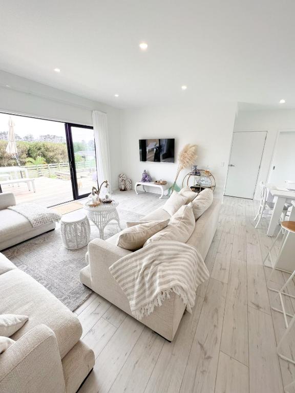 a living room with white furniture and a large window at Coastal Charm Escape in Karikari Peninsula