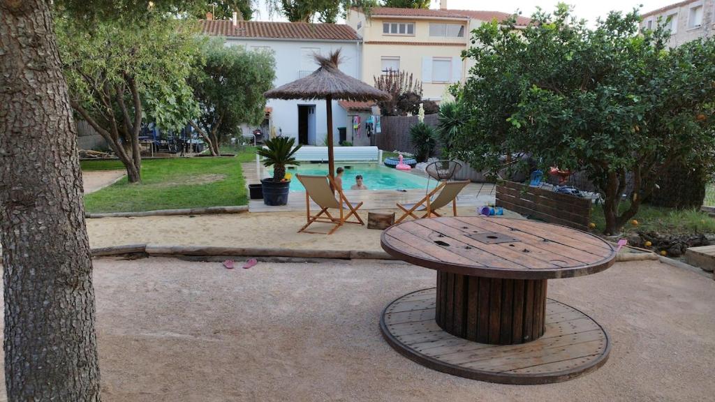 une table en bois assise à côté d'un arbre près d'une piscine dans l'établissement Maison, Piscine, à Rivesaltes