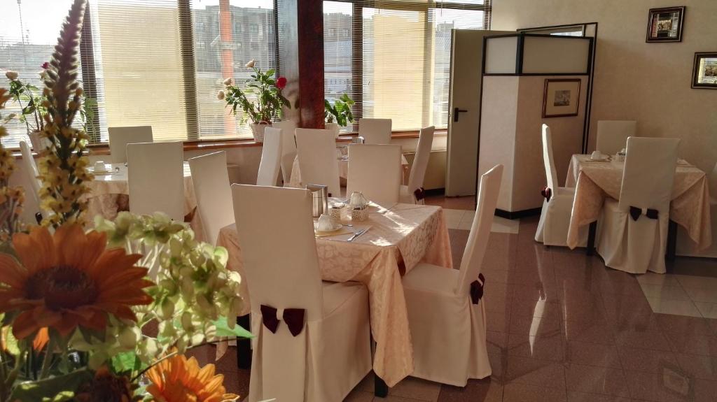 a restaurant with white tables and white chairs and flowers at Hotel Alexander in Cesena