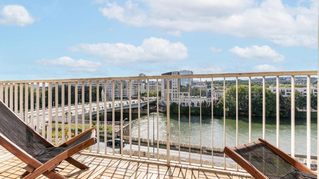 un balcon avec deux chaises et une vue sur l'eau dans l'établissement APPARTEMENT avec vue sur la Seine 10' en voiture de Paris et de la Tour Eiffel, à Boulogne-Billancourt