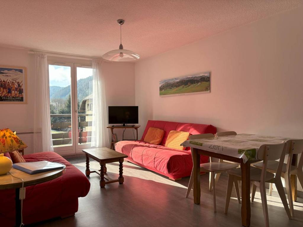 ein Wohnzimmer mit einem roten Sofa und einem Tisch in der Unterkunft Appartement cosy, balcon sud, 2 chambres, parking gratuit à 10 min du centre et proche ski ! - FR-1-548-4 in Villard-de-Lans
