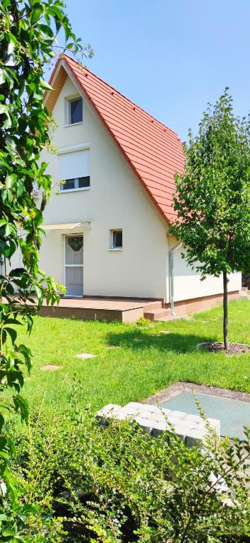 a white house with a red roof and a tree at Bathy Ház in Tiszakécske