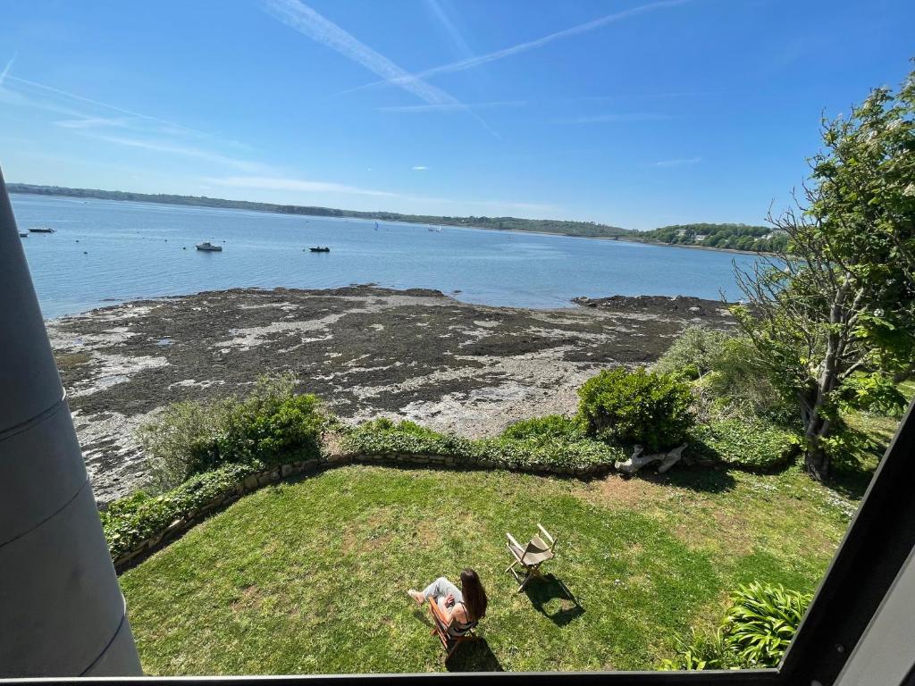 une femme assise sur l'herbe et regardant l'eau dans l'établissement Rare Grande Villa Incroyable vue mer, à Roscanvel