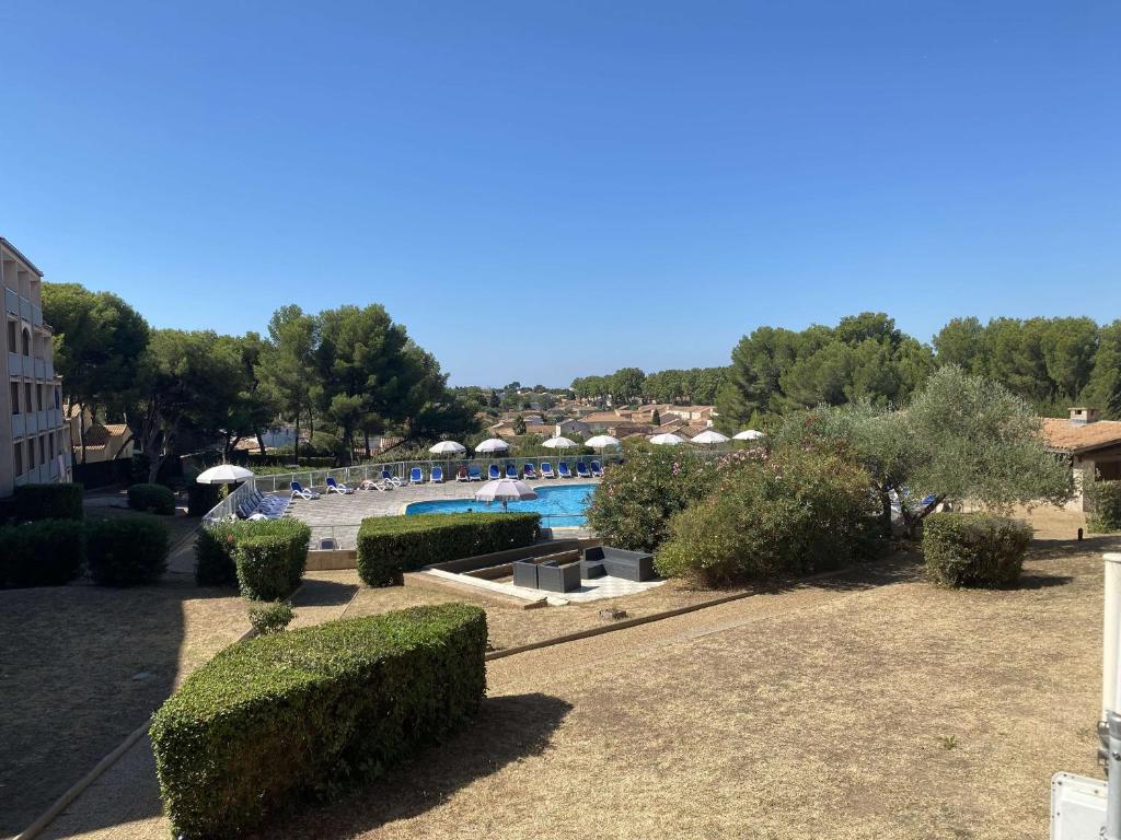 un complexe avec une piscine bordée de parasols et de buissons dans l'établissement Appartement 2 pièces avec terrasse et piscine à Balaruc-les-Bains - FR-1-553-286, à Balaruc-les-Bains