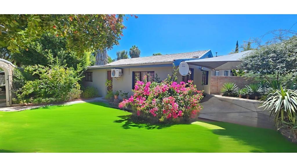 a house with a yard with green grass and flowers at Self-catering Garden Cottage in Oudtshoorn