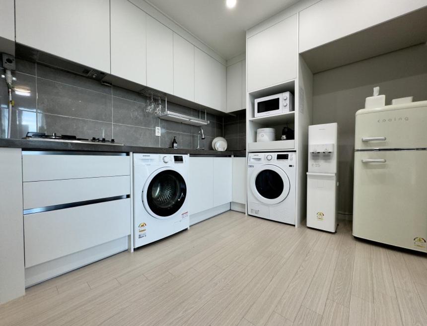 una cucina con mobili bianchi, lavatrice e asciugatrice di Eunhasu D&M Residence a Daejeon