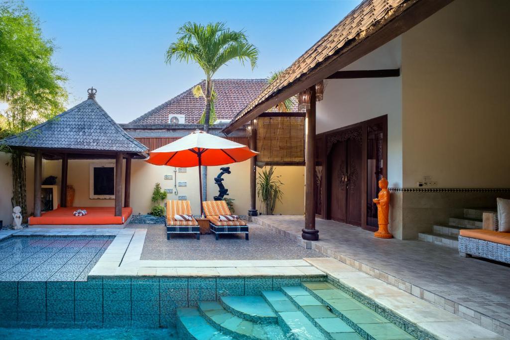 a pool with chairs and an umbrella next to a house at Villa Asyik in Seminyak