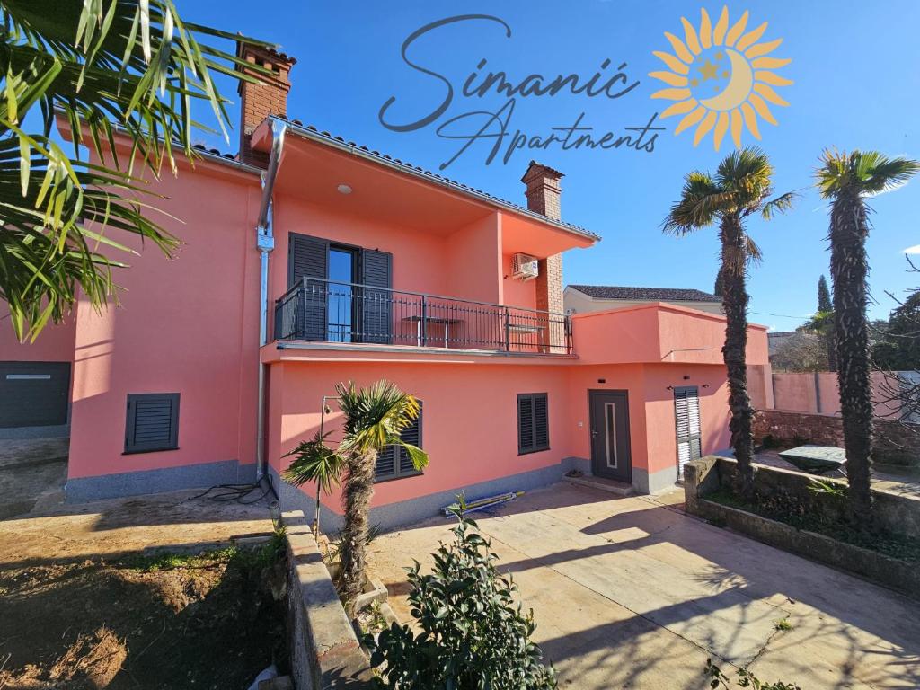 a pink house with palm trees in front of it at Simanić Apartments in Malinska