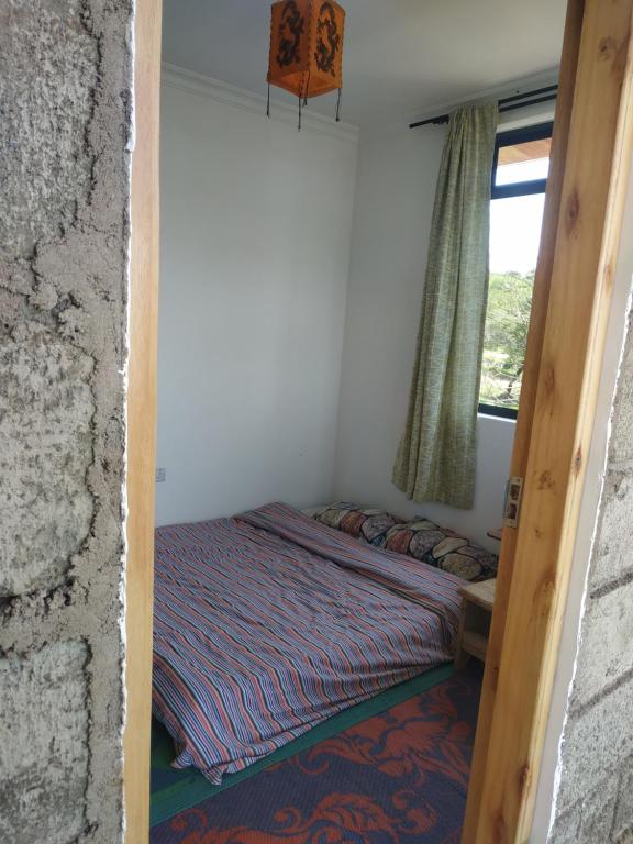 a bed in a small room with a window at Room With Balcony In Family Farm House UK Host in Arusha