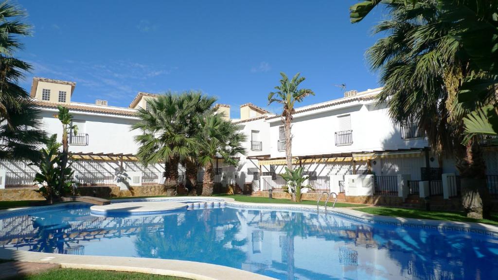 a swimming pool in front of a building with palm trees at Adosados Palm Beach Altamar in Alcossebre