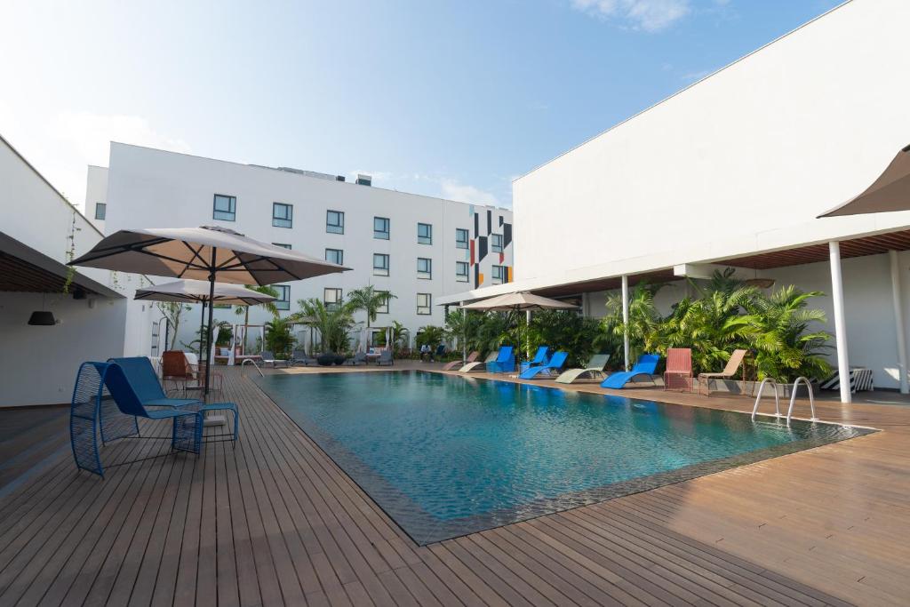 a pool with chairs and umbrellas next to a building at ONOMO Hotel Abidjan in Abidjan