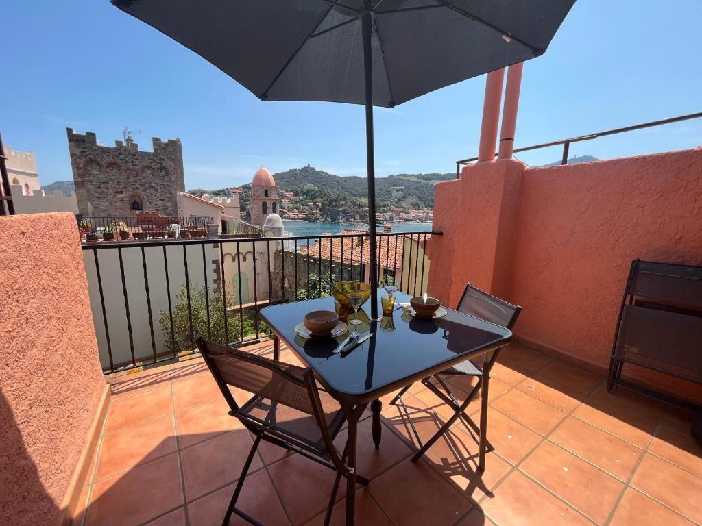 une table et des chaises sur un balcon avec un parasol dans l'établissement 3FAN4-Charmant appartement-Vue sur la mer et clocher de Collioure, à Collioure