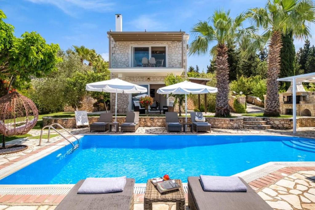 a villa with a swimming pool and palm trees at Villas Goudis in Tsoukaladhes
