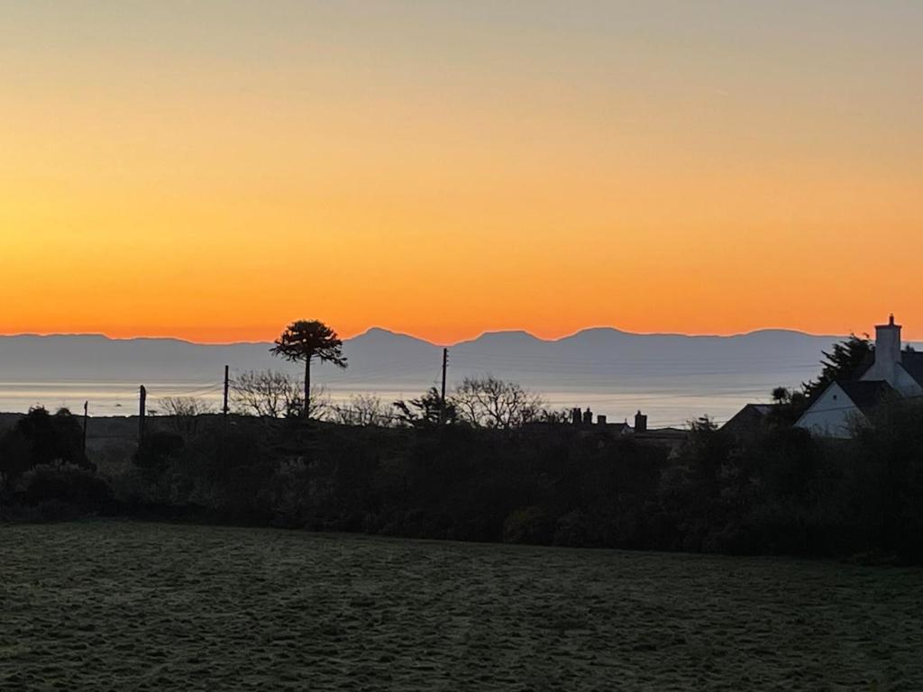 a sunset with a tree and mountains in the background at Studio room with amazing views in Abersoch