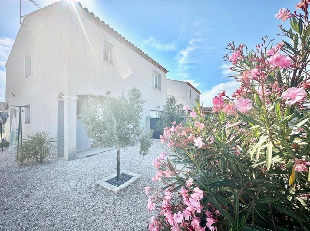 un bâtiment blanc avec des fleurs devant dans l'établissement Villa avec piscine privée, à Sallèles-dʼAude