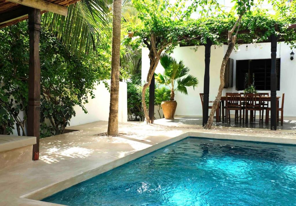 a swimming pool in front of a house with trees at Mwendawima Beach Villa in Jambiani