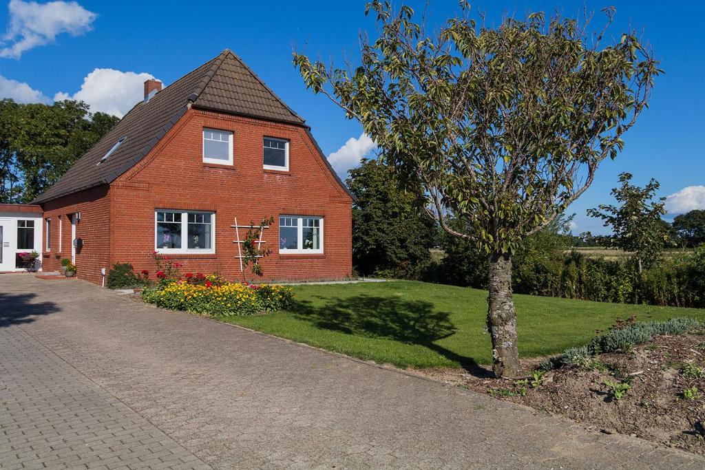 a red brick house with a tree in the yard at Norderhof Hansen - Ferienhaus in Nordstrand
