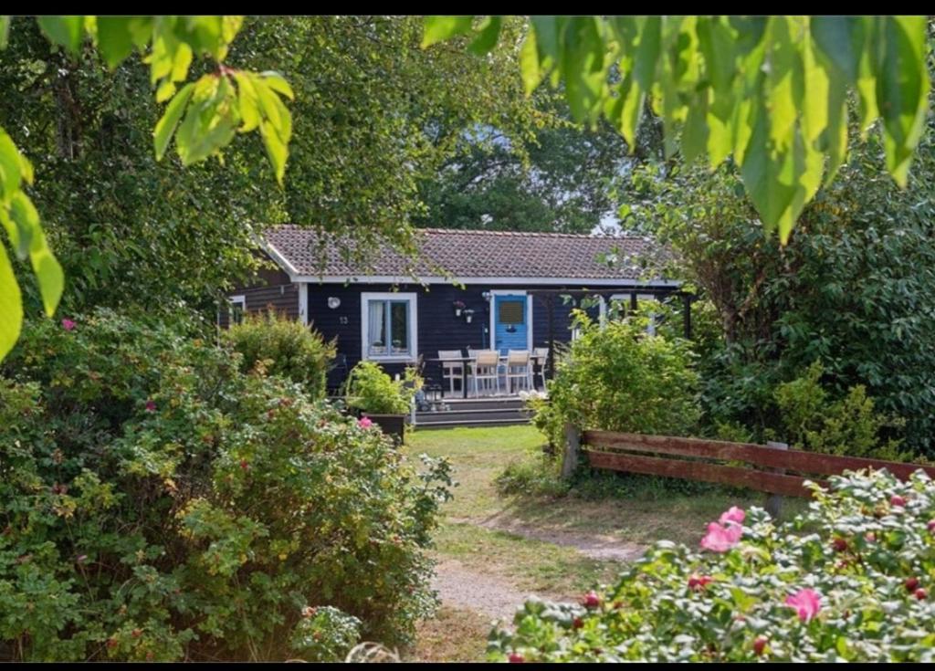 ein schwarzes Haus mit einer blauen Tür in einem Garten in der Unterkunft Sea Breeze Cottage in Färjestaden
