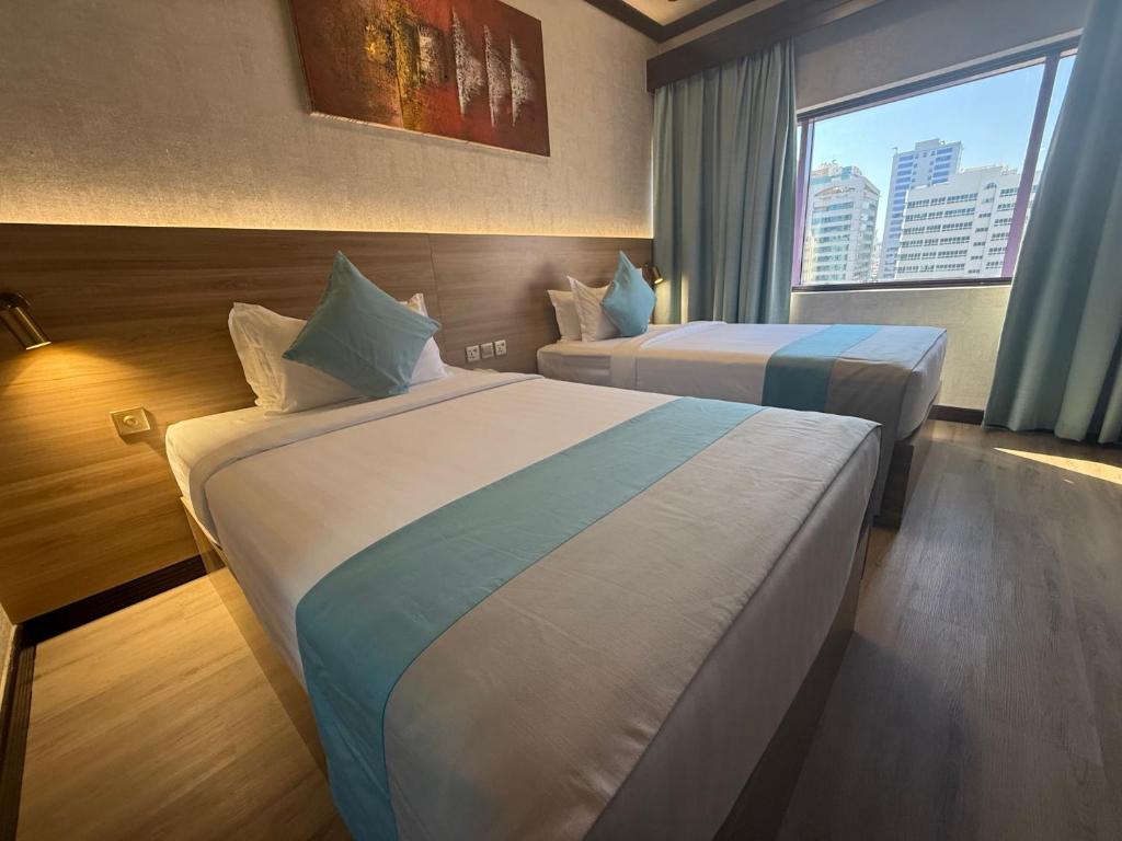 two beds in a hotel room with a window at Strand Hotel in Abu Dhabi