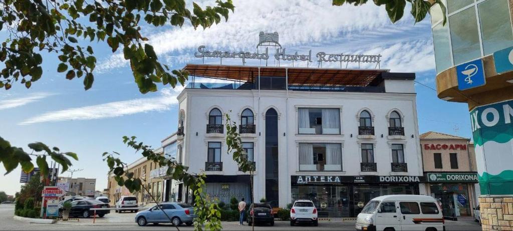 Un edificio blanco en una calle de la ciudad con coches aparcados. en Samarqand Darvoza, en Bukhara