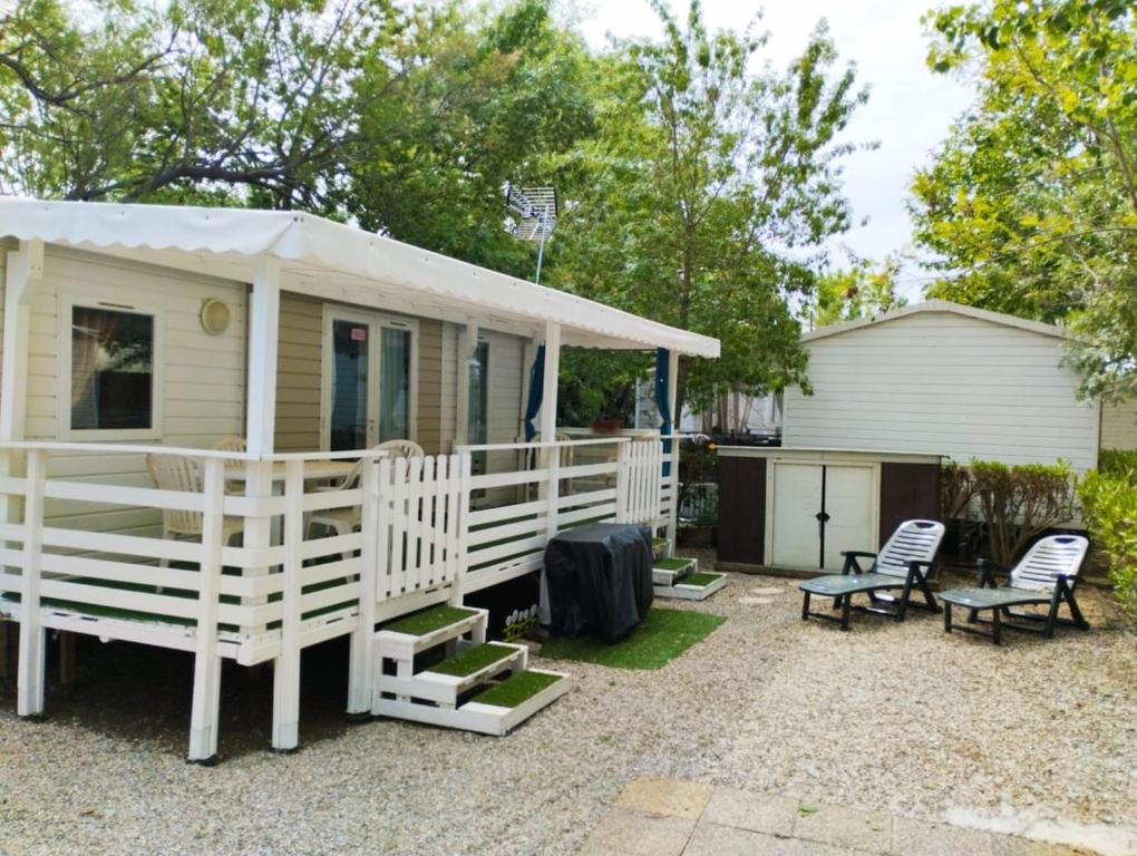 une petite maison avec une terrasse couverte et 2 chaises dans l'établissement Mobil-home CA 67 à Vias - La Carabasse - Camping Siblu avec piscine, à Vias