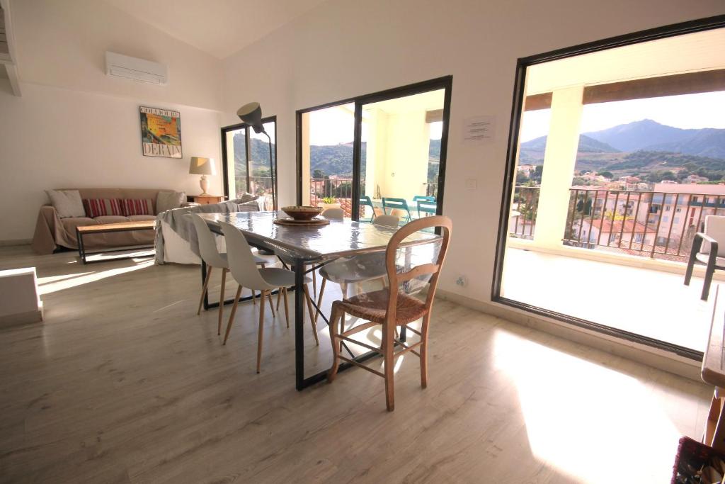 une salle à manger avec une table, des chaises et des fenêtres dans l'établissement Belvédère, à Collioure