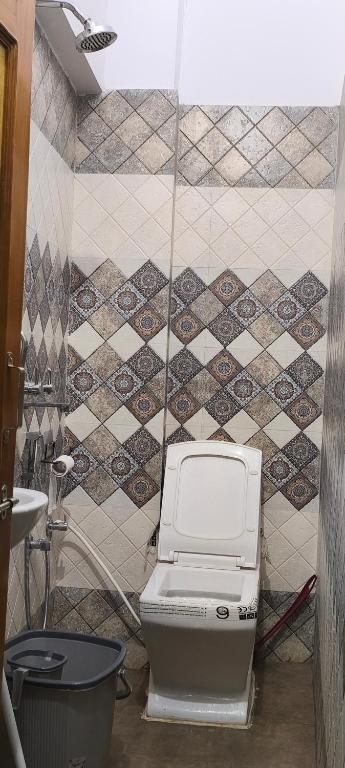 a toilet in a bathroom with a tiled wall at Rose Merry Guesthouse in Bikaner