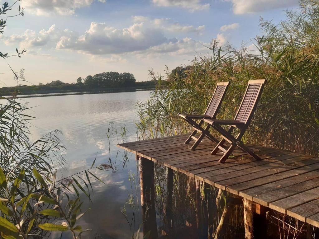 due sedie sedute su un molo accanto a un corpo d'acqua di Ferienhaus am grossen See in Fuerstenwerder a Fürstenwerder