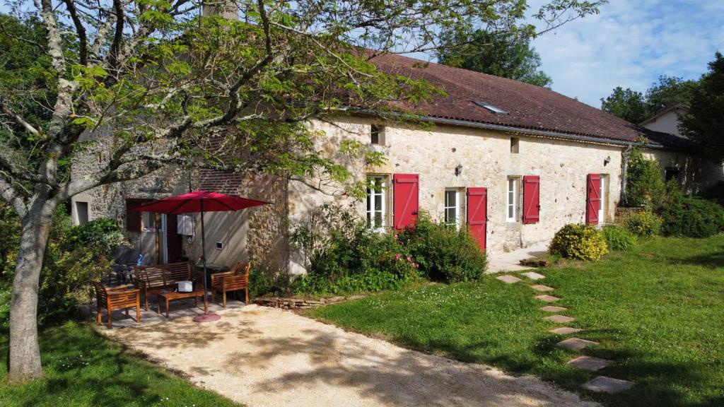 una casa di pietra con porte rosse, un tavolo e delle sedie di La Ferme de Belbouys a Soturac