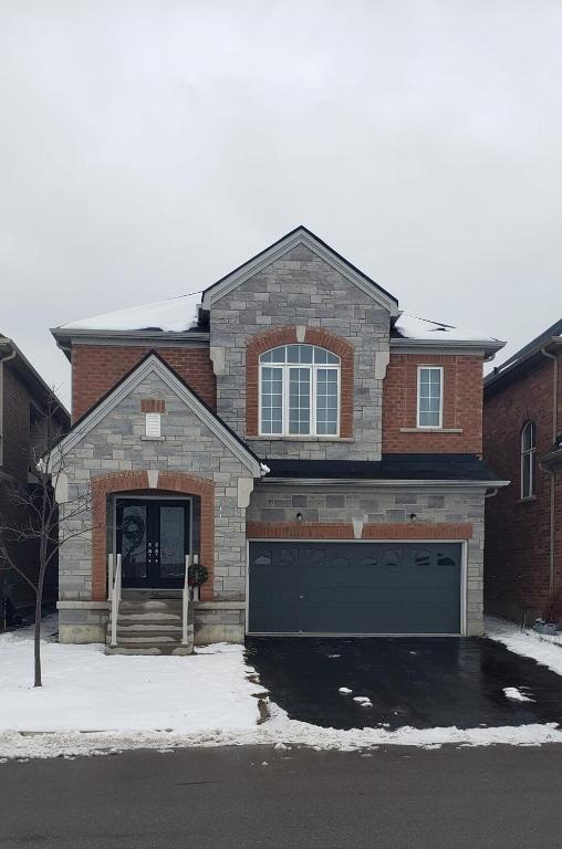 a brick house with a garage in the snow at Velohome - 3-Bed, 2-Bath Home in Milton